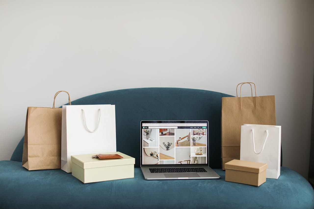 A laptop surrounded by shopping bags and boxes on a blue sofa, ideal for online shopping themes.