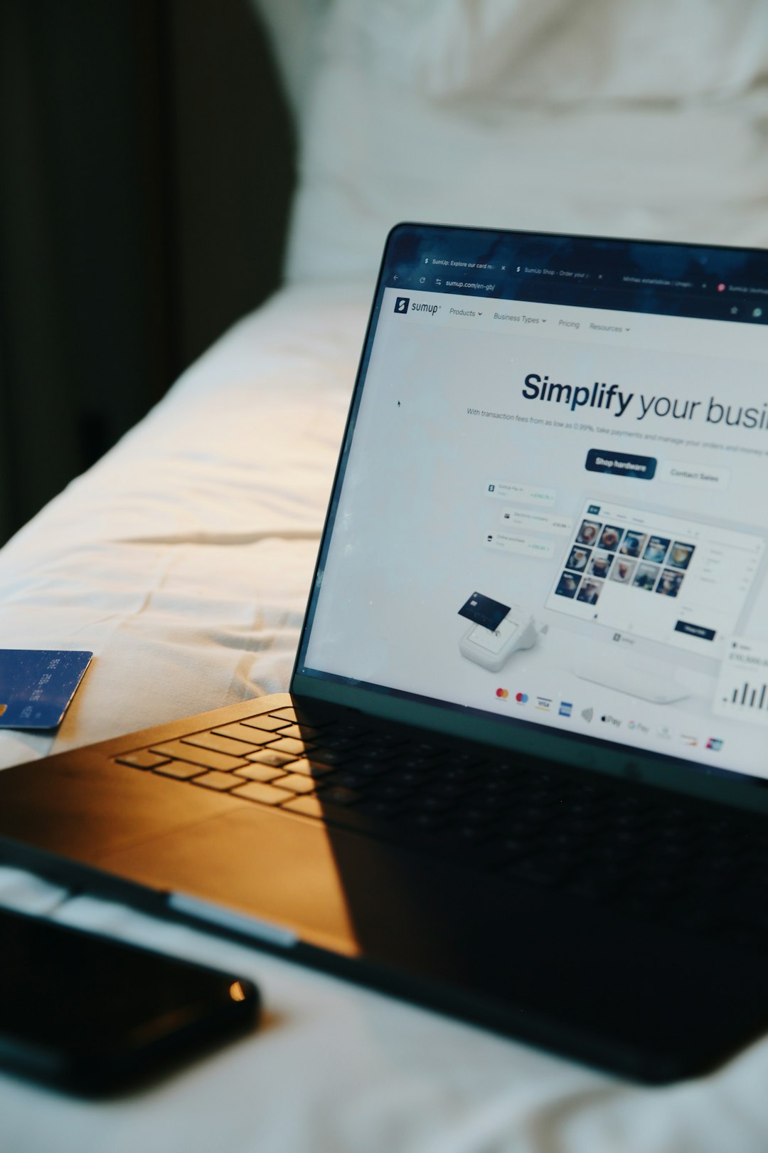 Laptop displaying the SumUp website on a bed, with soft natural light and a credit card nearby. A visual representation of remote business management, online sales, and the flexibility of running a digital-first company from anywhere.